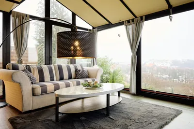 Gemütlicher Wintergarten mit Blick auf die Natur. Heller Raum mit Sofa, Teppich und Tisch.